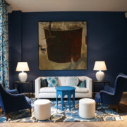 lichte kamer met witte bank, groot raam met bloederige gordijnen en vloerkleed, blauwe muren en blauwe salontafeltje