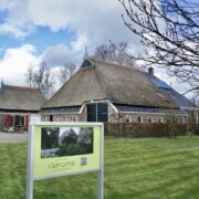 Rietgekapte grote boerderij in grasveld met een een aangebouwde kleinere 'stal'