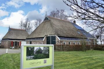 Rietgekapte grote boerderij in grasveld met een een aangebouwde kleinere 'stal'